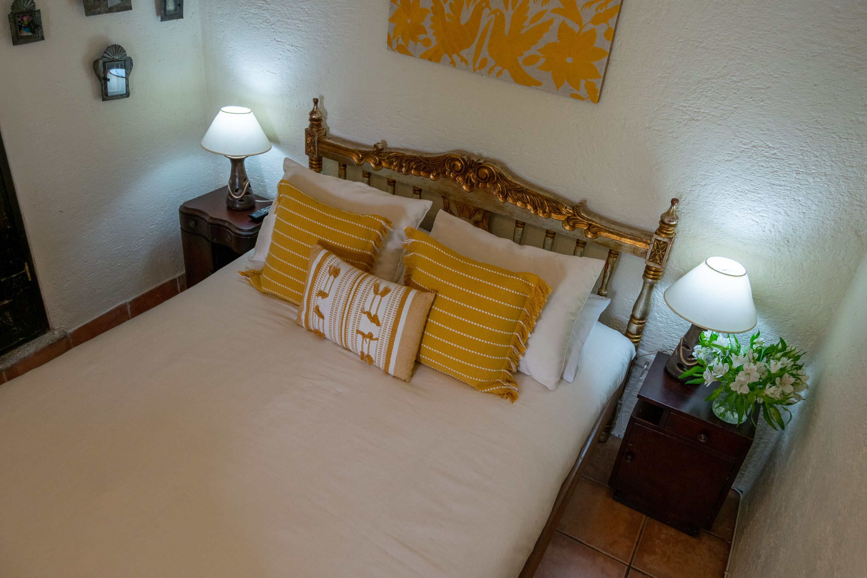 A neatly made bed with white and yellow striped pillows, a wooden headboard, and two bedside tables with lamps and a vase of flowers.