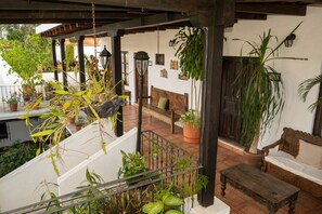 A covered outdoor seating area with a wooden bench, a table, and potted plants. - La Villa Serena  (Antigua Guatemala)