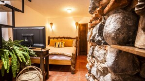 Un dormitorio acogedor con cama, televisor, una mesa de madera y una pared de piedra.