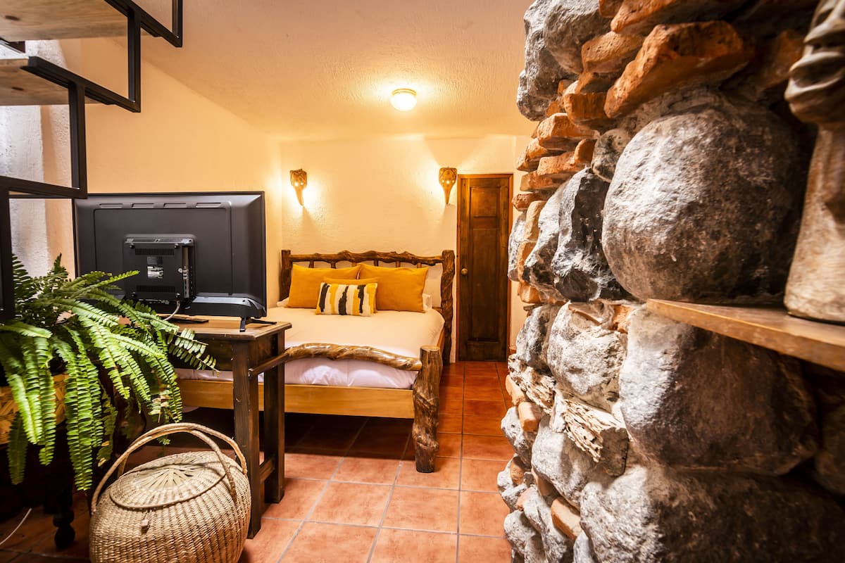 Un dormitorio acogedor con cama, televisor, una mesa de madera y una pared de piedra.