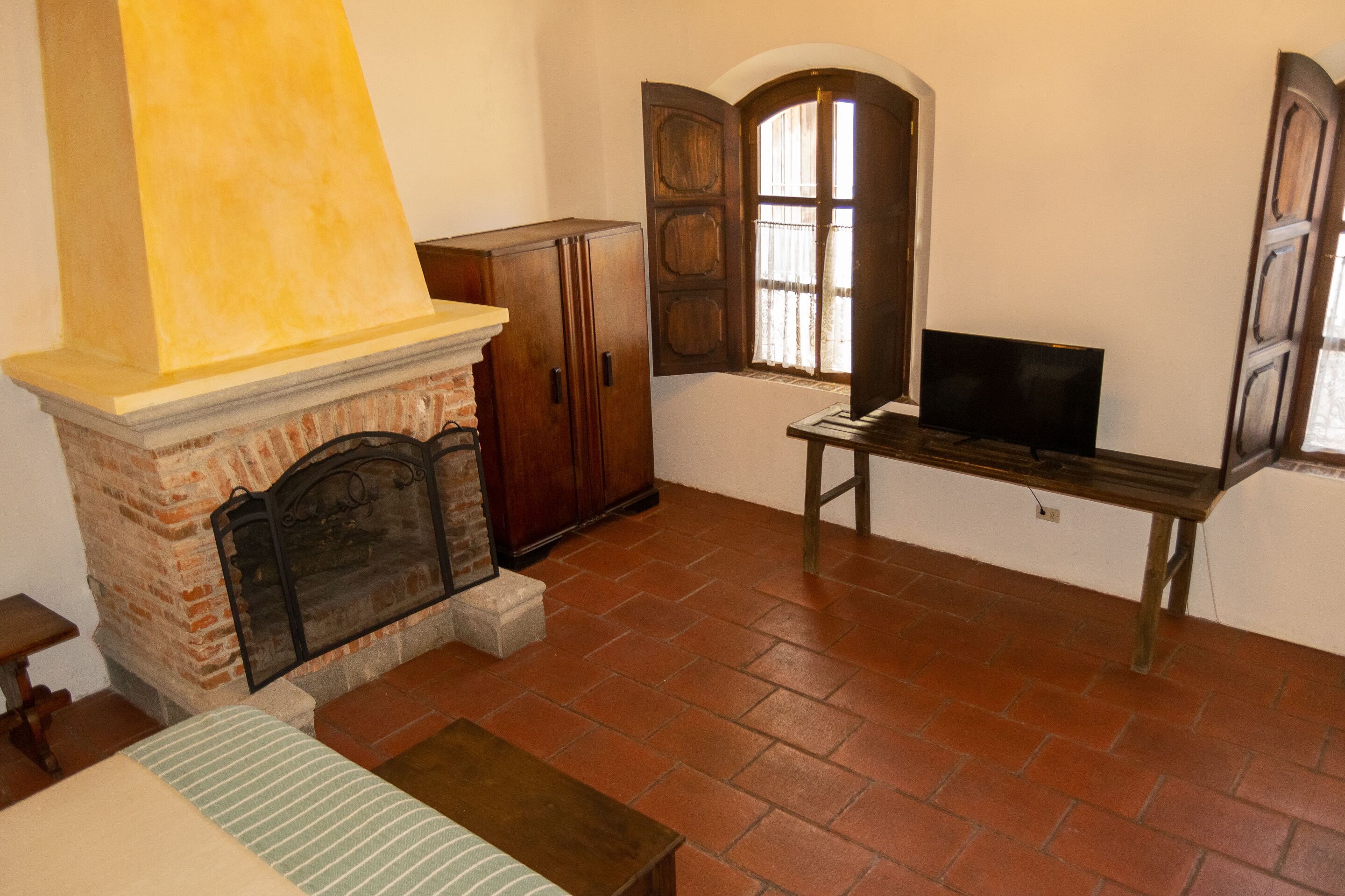 Ein Zimmer mit Kamin aus Ziegelsteinen, Holzschränken, einem Fernseher auf einem Holztisch und einem Fenster mit Vorhängen.