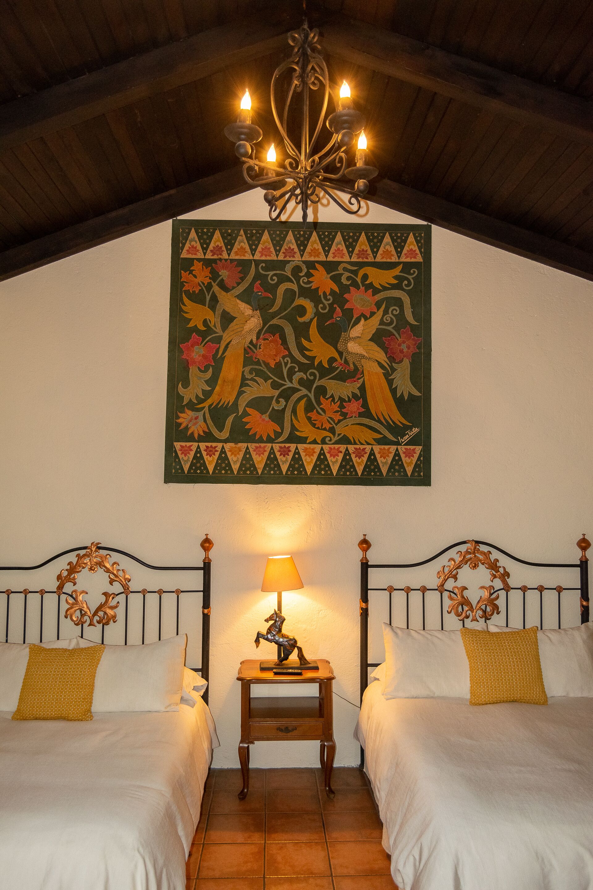 Une chambre avec deux lits, un lustre, une décoration murale et une table de chevet avec une lampe.