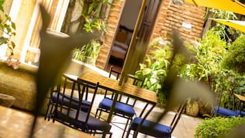 Een terras buiten met een houten tafel en blauwe stoelen, omringd door potplanten en een bakstenen muur.