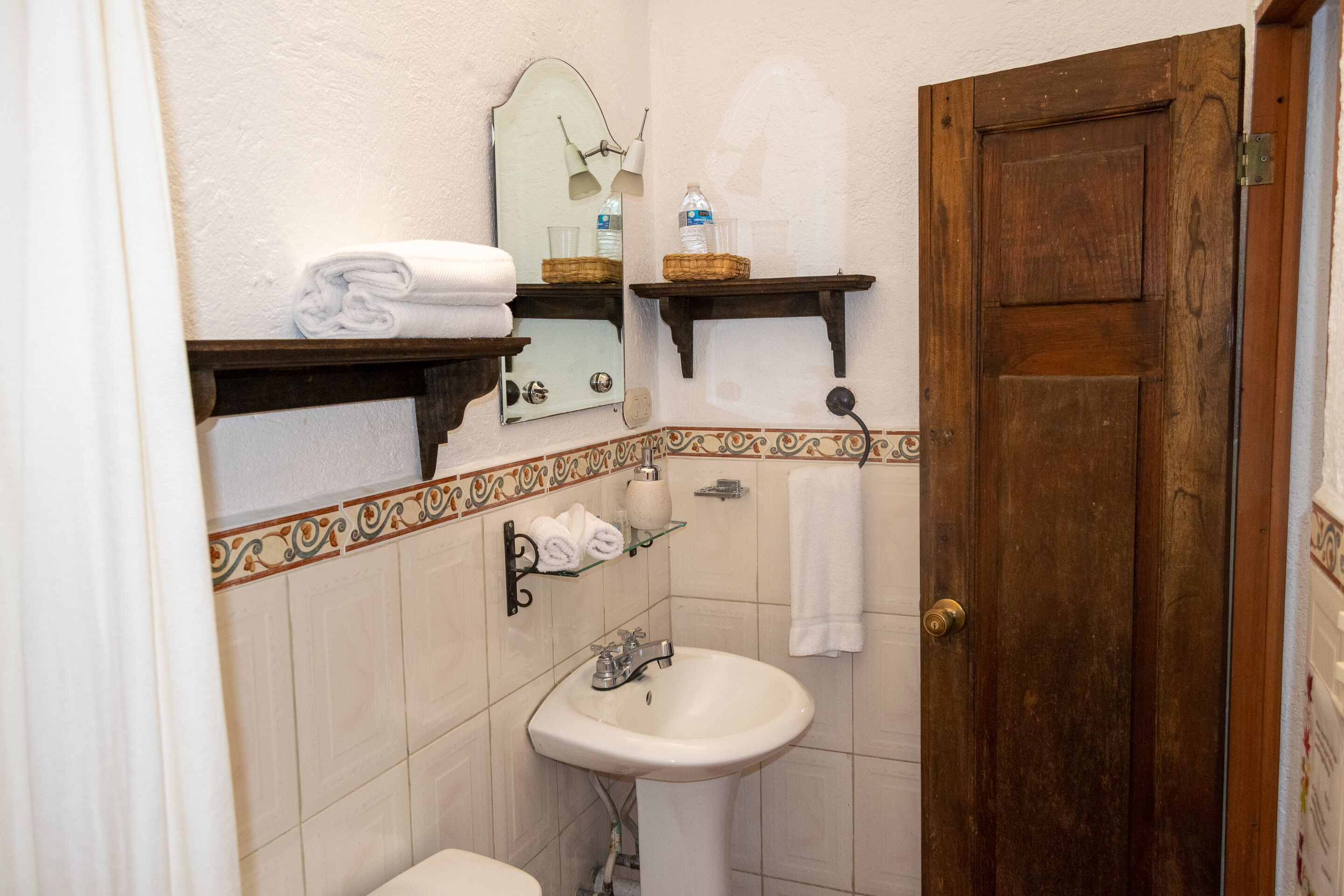A bathroom with a sink, mirror, towel rack, and wooden door.