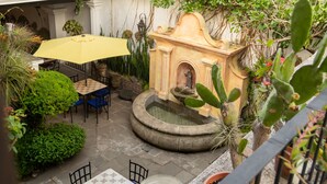 Un patio al aire libre con una fuente, mesas, sillas y plantas en macetas.