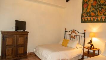 A bedroom with two beds, a wooden cabinet, a television on top, and a decorative wall hanging.