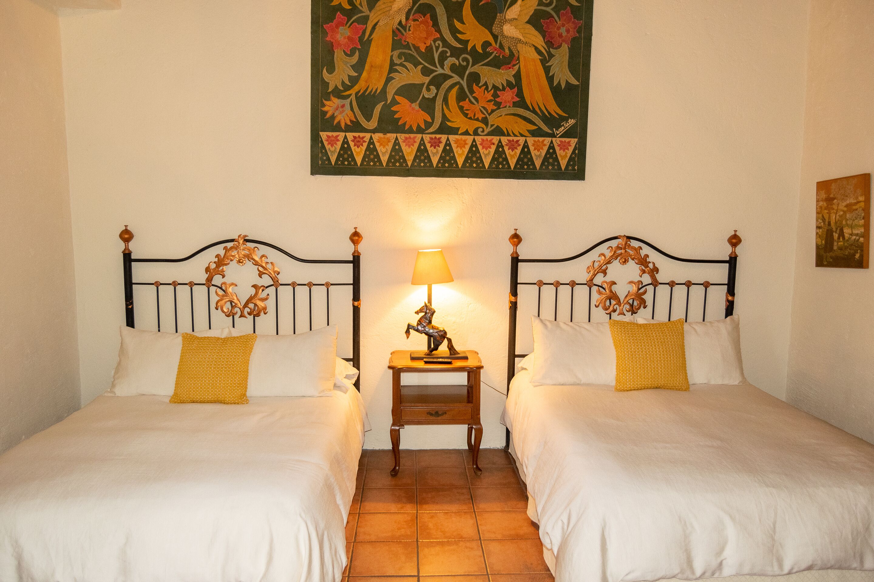 A hotel room with two beds, a nightstand with a lamp, and a decorative wall hanging.
