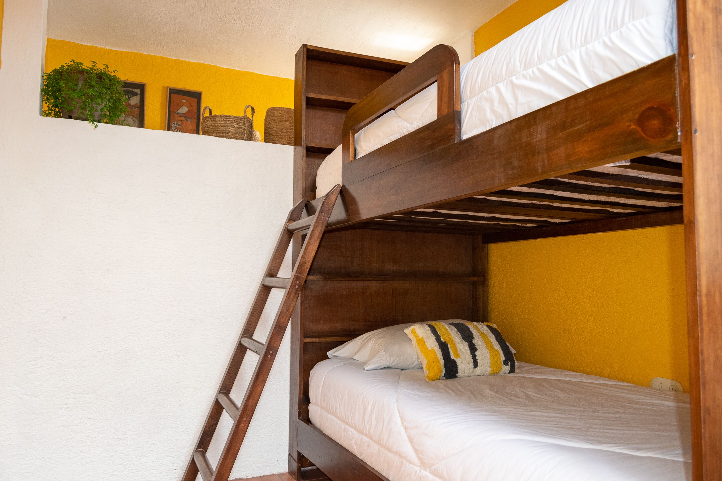 A bunk bed with a ladder, white bedding, and a yellow wall.