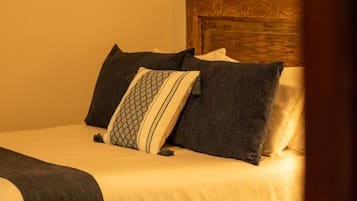 Una cama bien hecha con tablero de madera, ropa de cama blanca y oscura, y una almohada estampada.