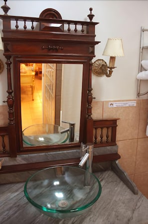 A bathroom with a wooden vanity, a glass sink, and a mirror. - Majoro (Canaria)