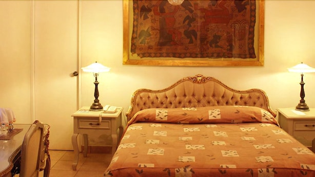 Une chambre d’hôtel avec un grand lit, deux tables de chevet avec des lampes, un bureau avec une chaise et une grande tapisserie au mur.