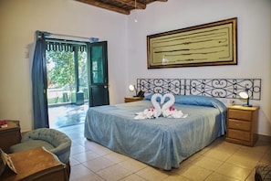 A bedroom with a bed, a nightstand, a chair, a door leading outside, and a wall with a framed artwork. - Majoro (Canaria)