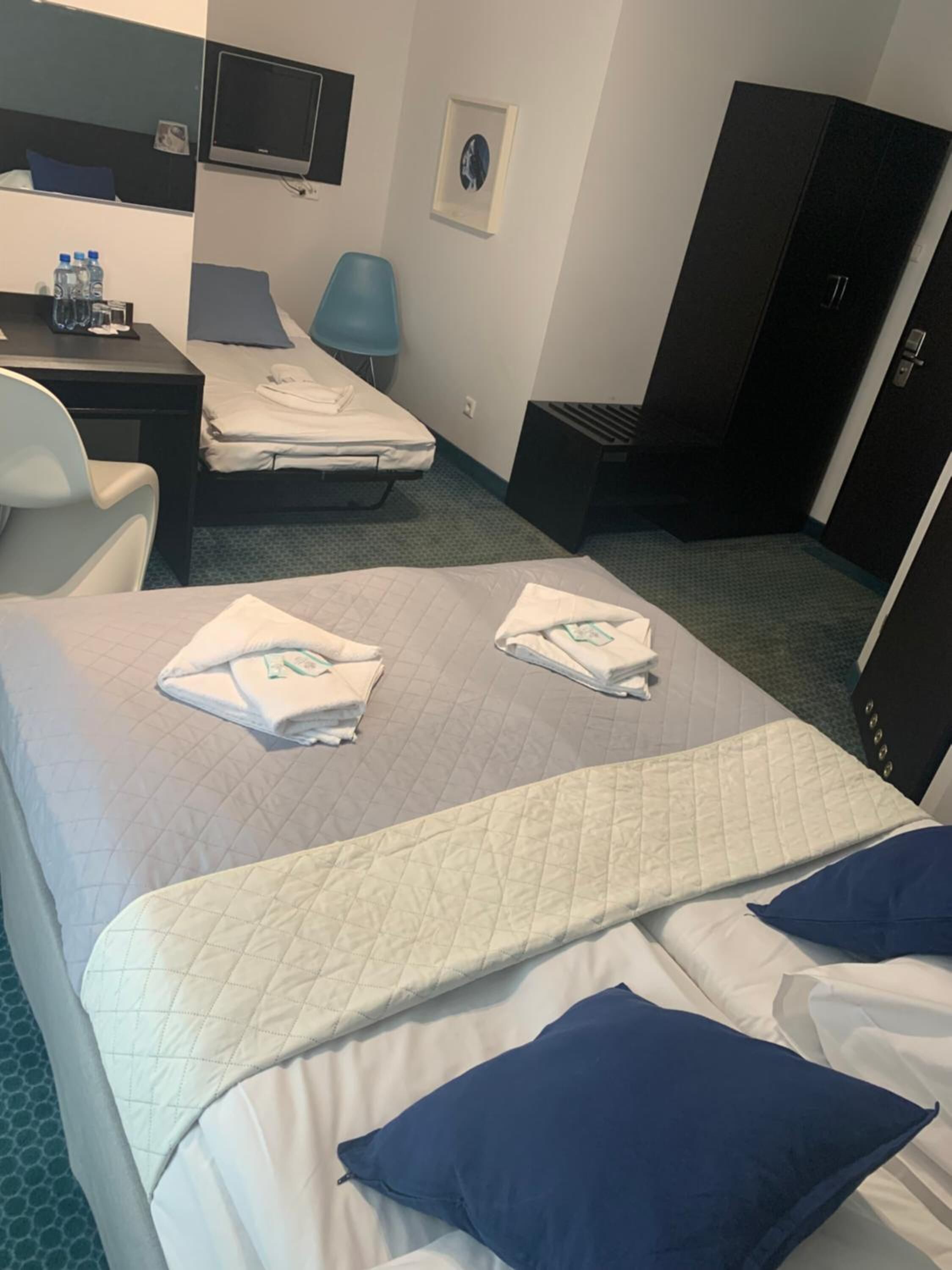A hotel room with two beds, a desk with a chair, a TV, and a wardrobe.
