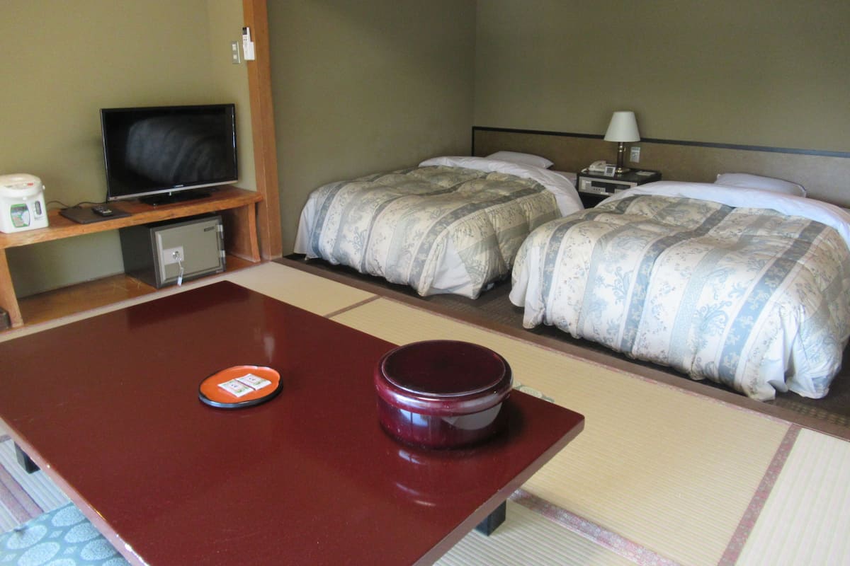 A hotel room with two beds, a television, a small desk, and a table with a bowl.