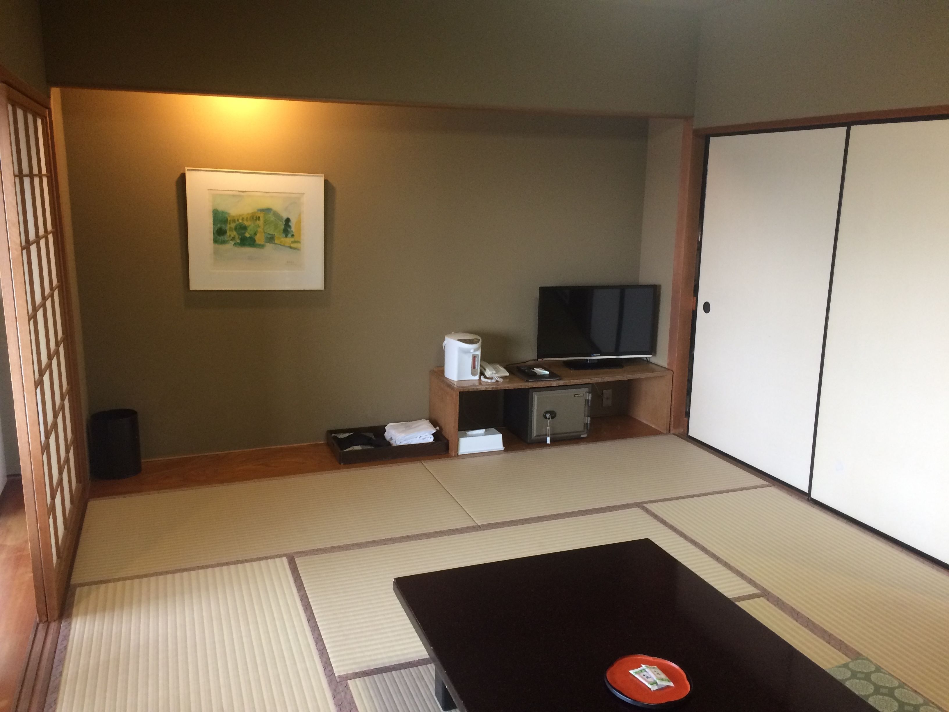 A room with tatami flooring, a black table, a television, a safe, and a framed picture on the wall.