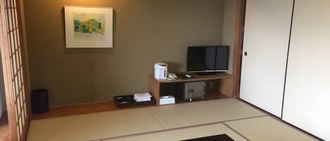 A room with tatami flooring, a black table, a television, a safe, and a framed picture on the wall.