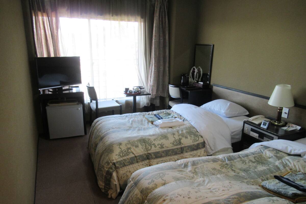 A hotel room with two beds, a desk, a television, and a small refrigerator.