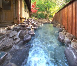 A clear water stream with large rocks lining the sides, a wooden fence, and a building with a traditional design. - Kikuchi Kanko Hotel (Kikuchi)