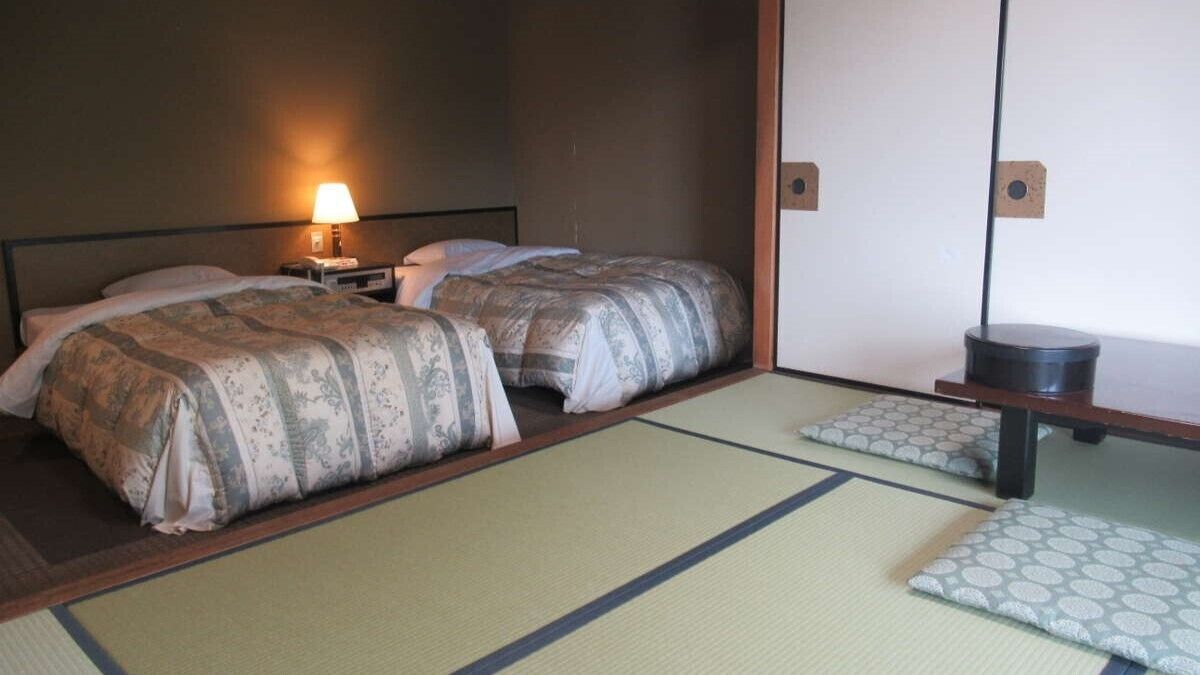 A room with two beds, a nightstand with a lamp, a wooden cabinet, and tatami mats.
