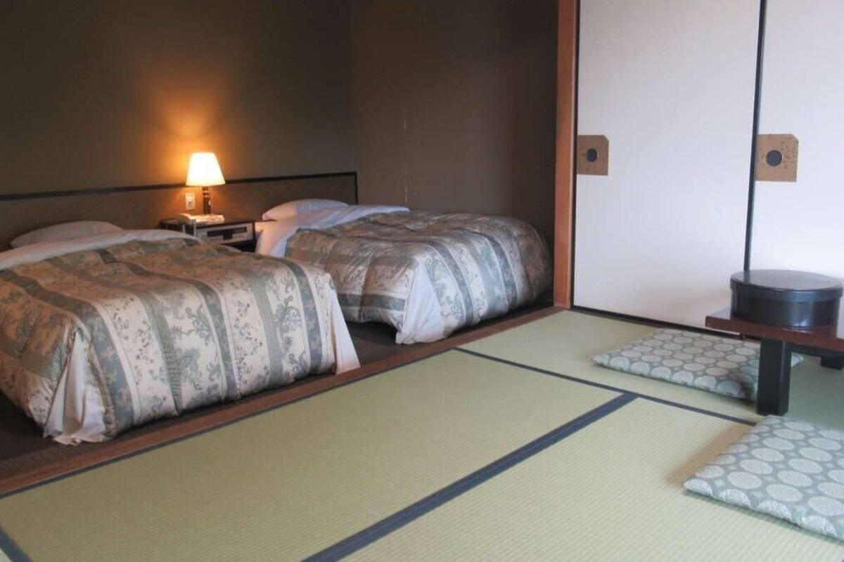 A room with two beds, a nightstand with a lamp, a wooden cabinet, and tatami mats.