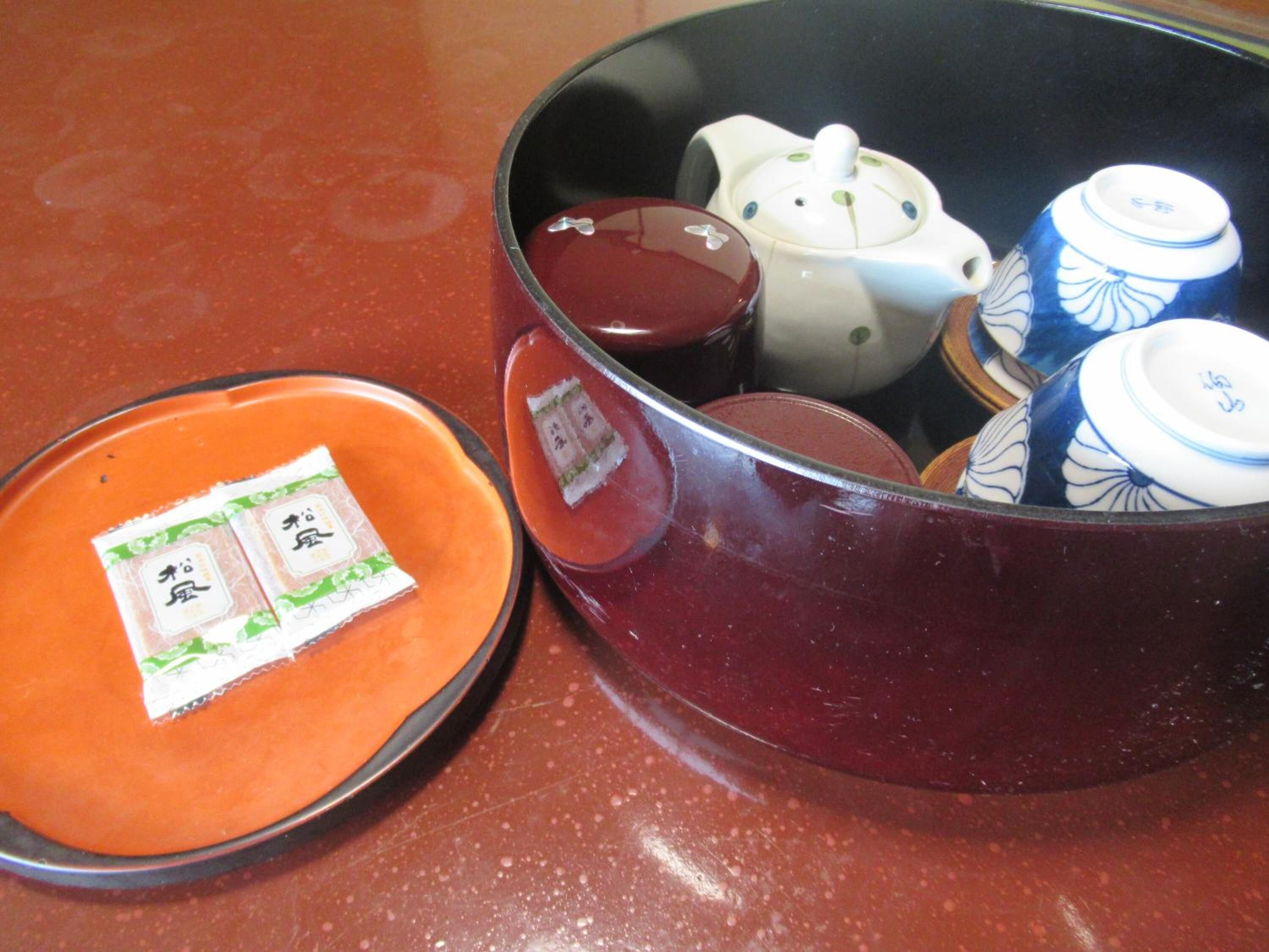 Una cocina con una olla roja, una tetera blanca y un juego de tazas de té azul y blanco.