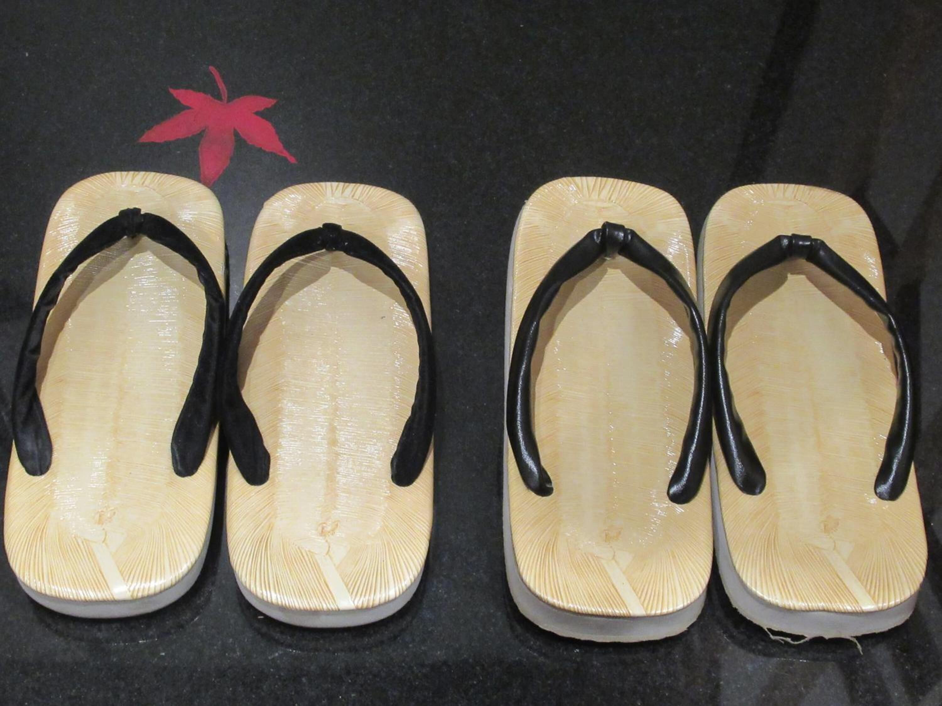 Four pairs of flip-flops with black straps and a wooden sole, arranged on a dark surface.