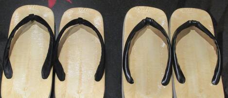 Four pairs of flip-flops with black straps and a wooden sole, arranged on a dark surface.