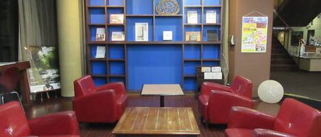 A lobby with a wooden table, red chairs, a blue wall with shelves, and a staircase in the background.