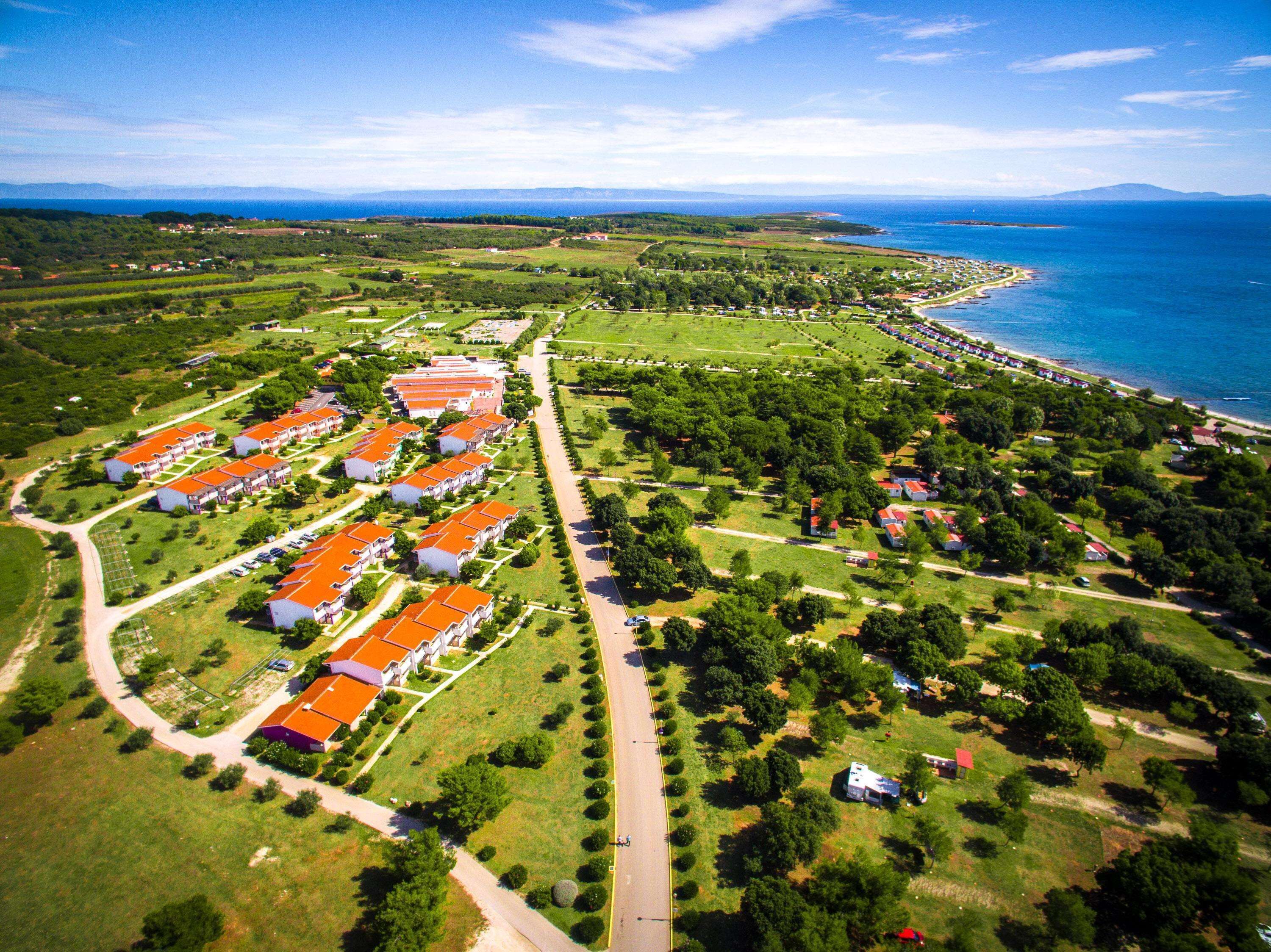 An aerial view of a coastal resort with multiple buildings, a well-maintained lawn, and a beach.