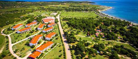 An aerial view of a coastal resort with multiple buildings, a well-maintained lawn, and a beach.