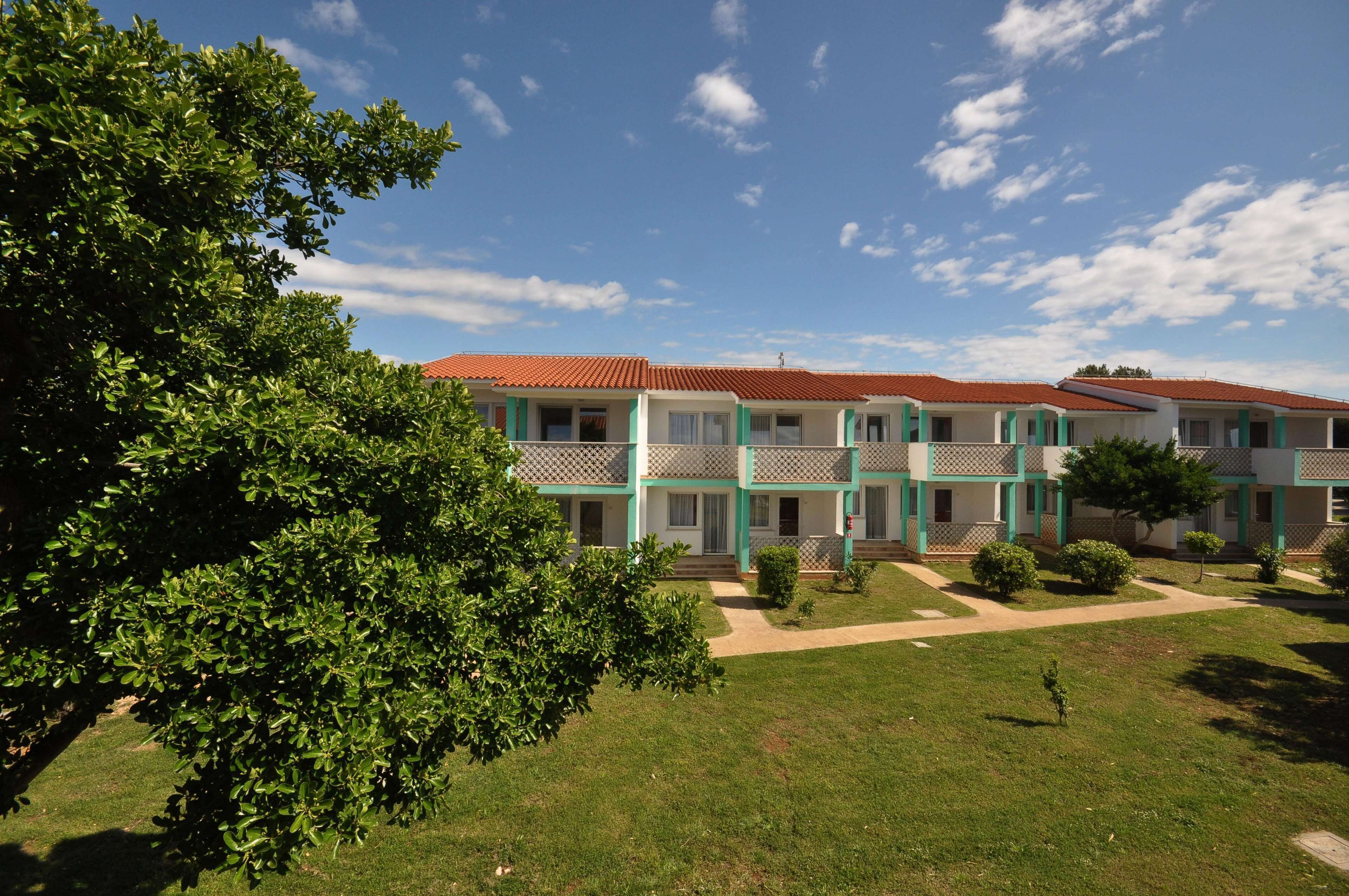 A multi-story building with a red-tiled roof, green accents, and a well-maintained lawn.