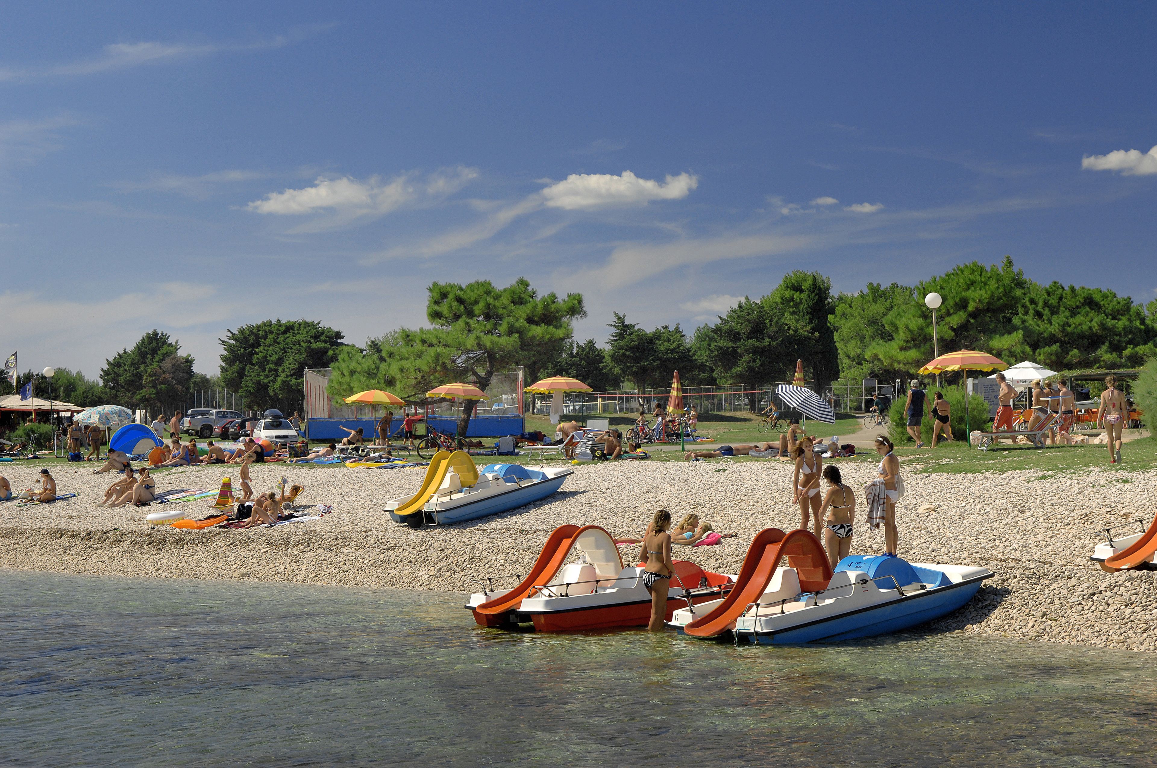 Une plage avec des bateaux, des parasols et des gens.