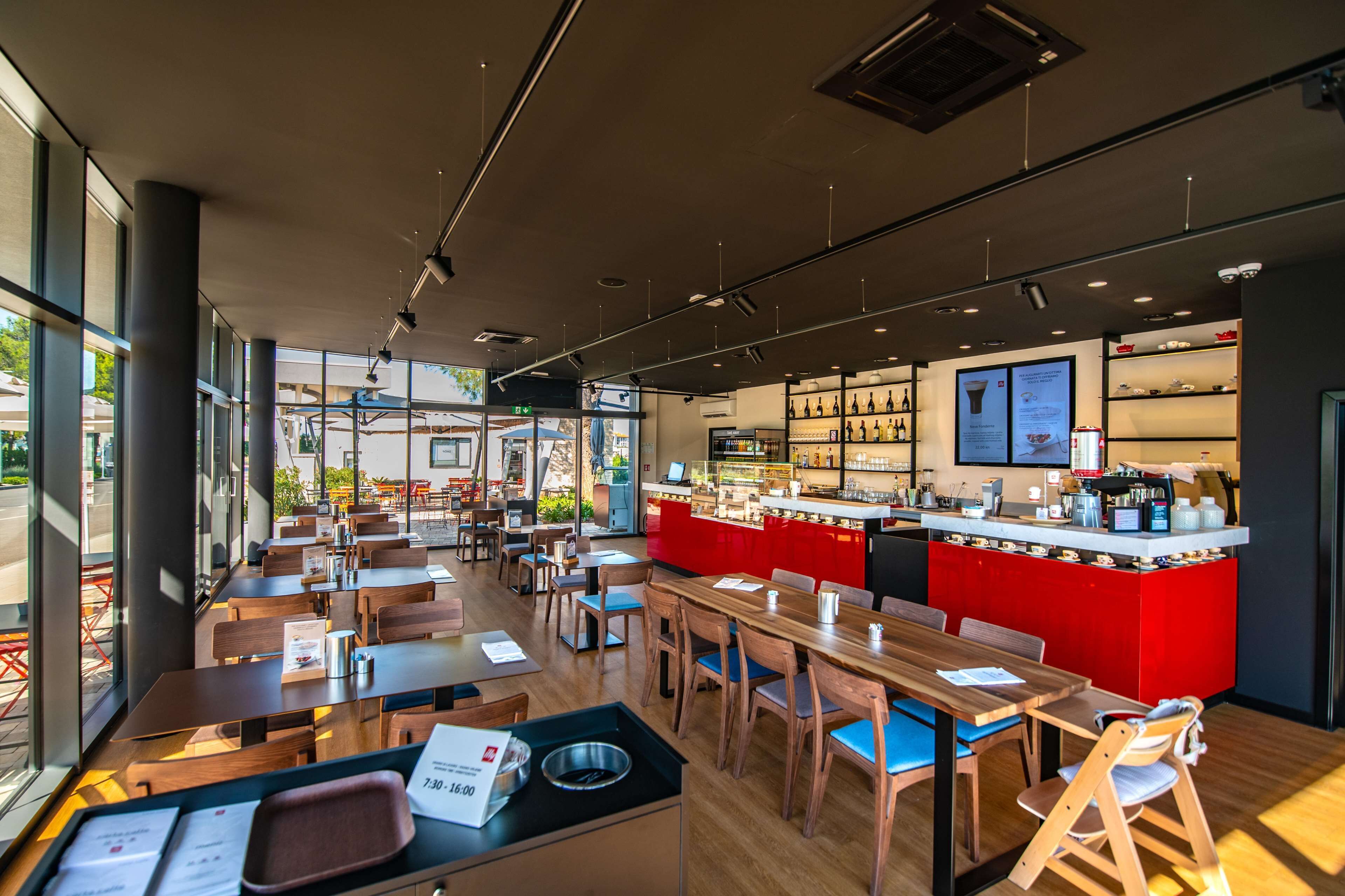 Un café moderne avec des tables et des chaises en bois, un comptoir rouge et une vue sur la rue.