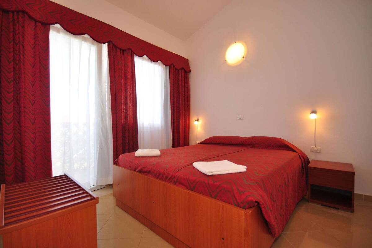 A bedroom with a wooden bed, red curtains, two bedside lamps, and a wooden nightstand.