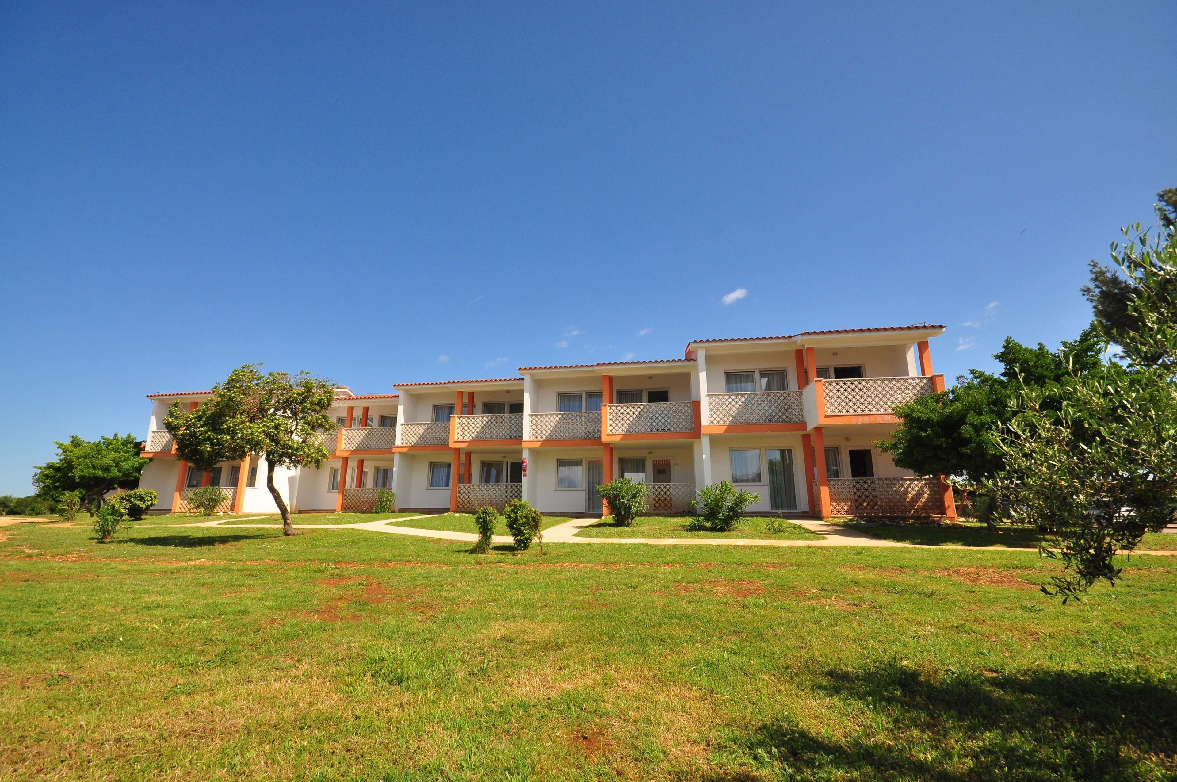 A multi-story residential building with balconies, a well-maintained lawn, and a clear blue sky.