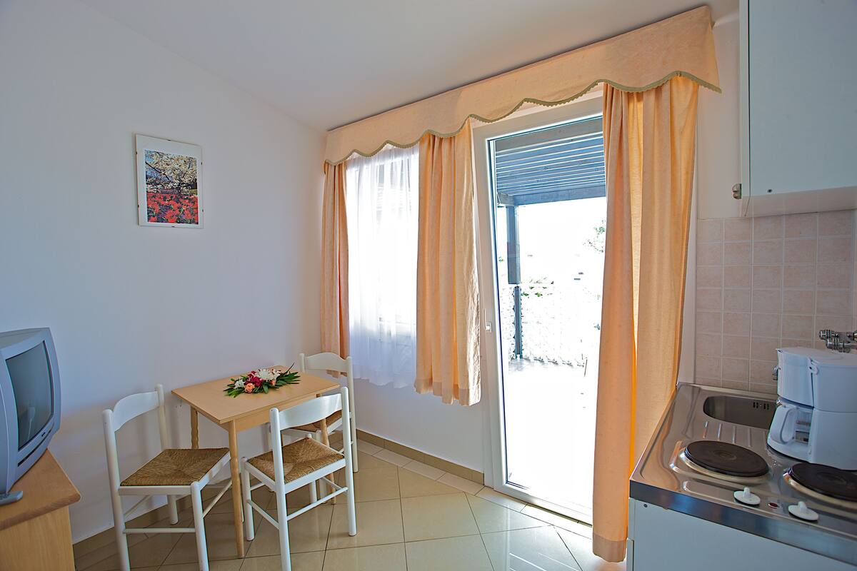 A small kitchen with a dining area, a television, and a window with curtains.