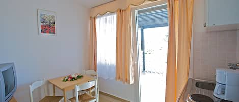 A small kitchen with a dining area, a television, and a window with curtains.