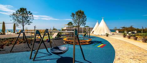 A playground with swings, a circular play area, and a white tent structure.