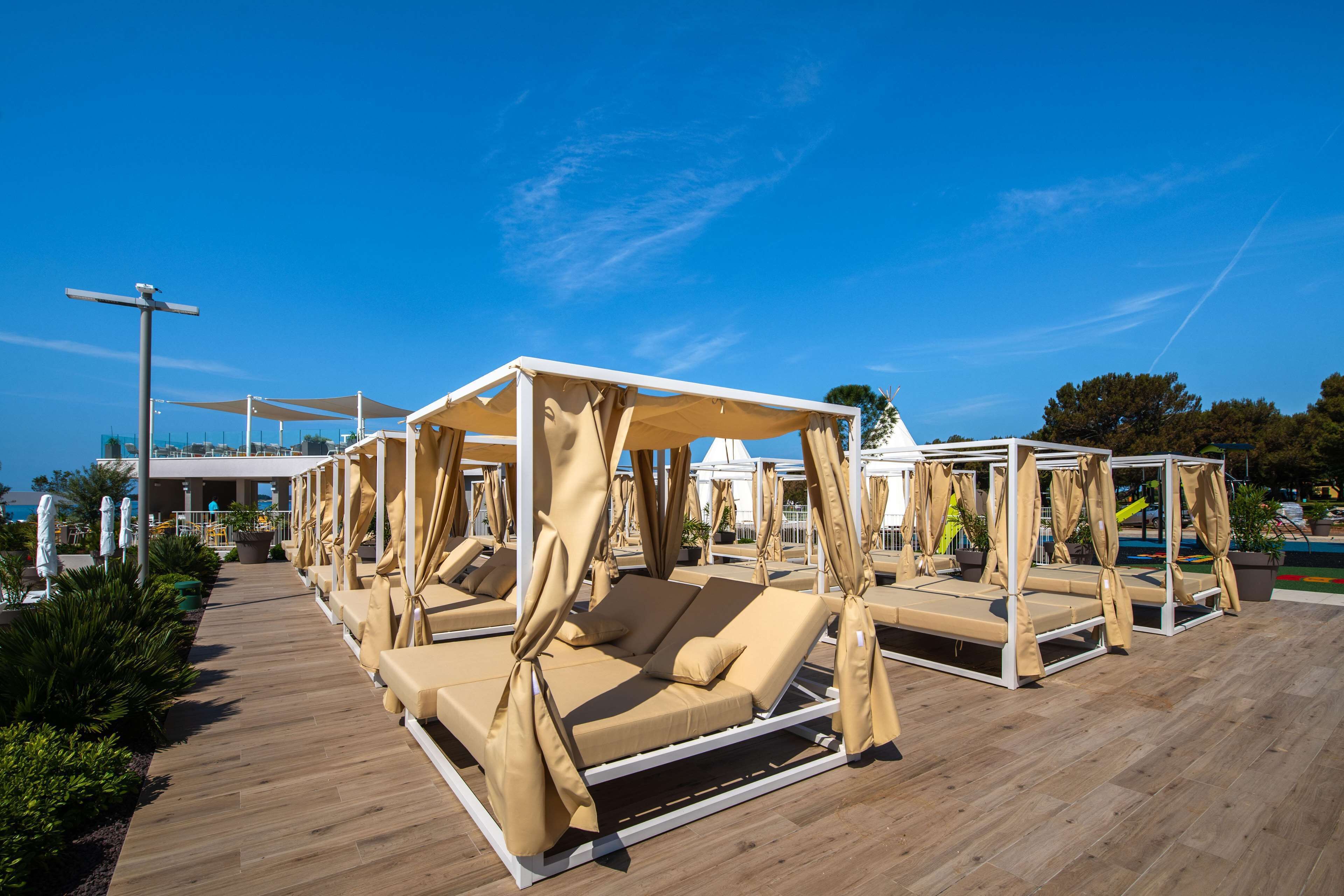 Des fauteuils de jardin dotés de toiles d’ombrage, une terrasse en bois et un ciel d’un bleu limpide.