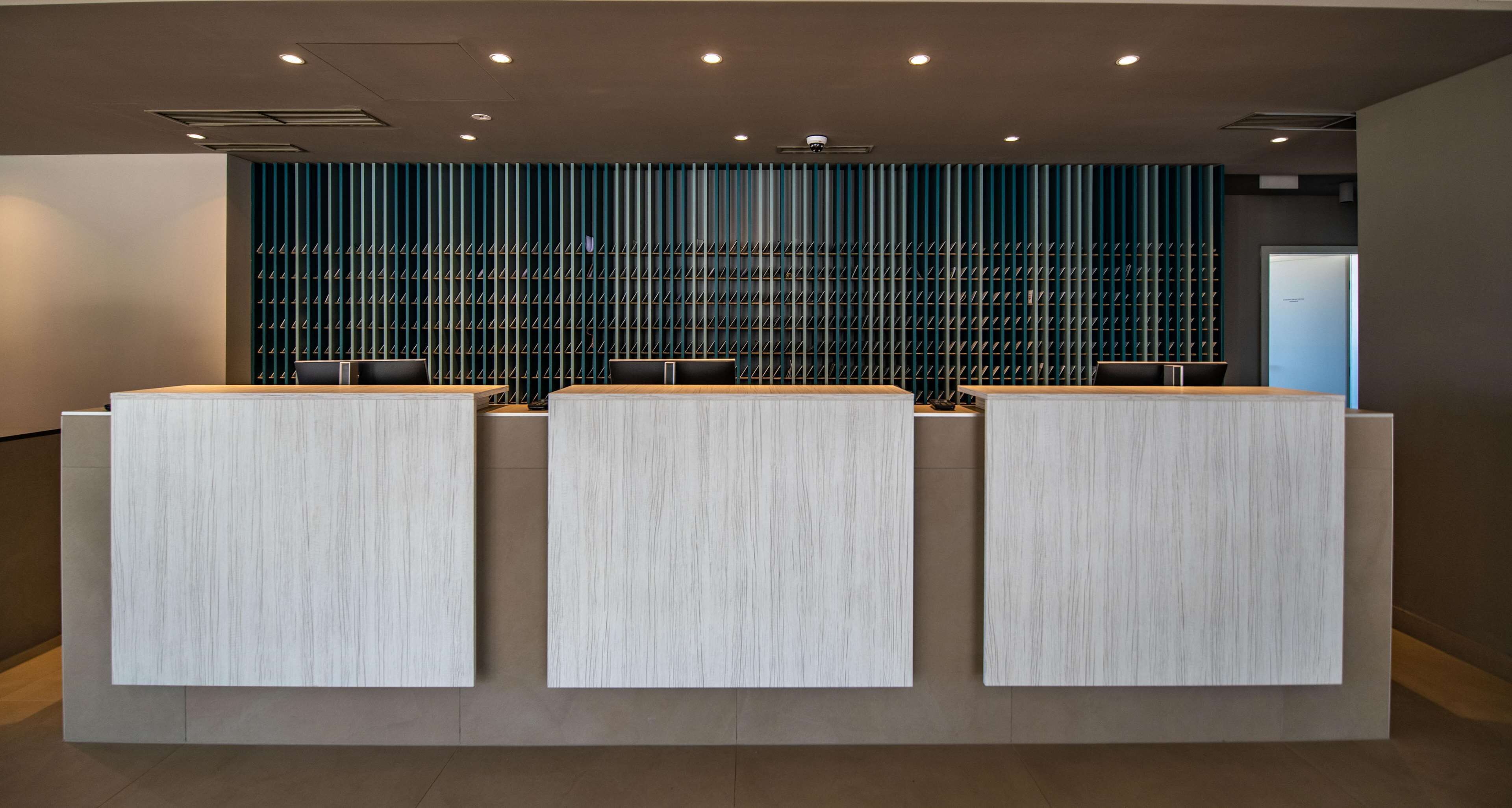 A reception area with three wooden reception desks, a blue acoustic panel wall, and recessed ceiling lighting.