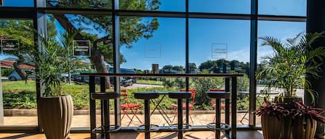 Un espace de détente intérieur moderne, doté de grandes fenêtres, de plantes en pot et offrant une vue sur l’extérieur.