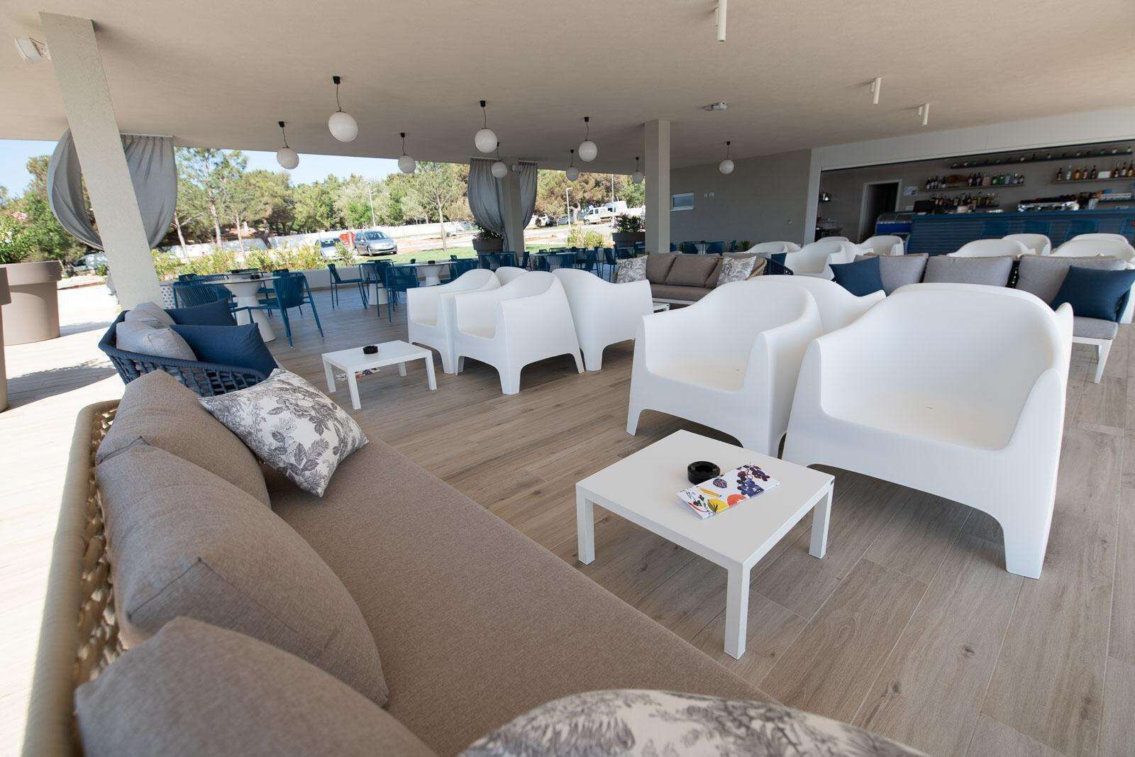 Un vaste espace de détente extérieur, doté de mobilier blanc, d’un plancher en bois et offrant une vue sur le paysage environnant.