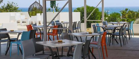 Un espacio de estar al aire libre con mesas y sillas, con vistas al mar.
