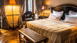 Una habitación de hotel bien iluminada con una cama grande, una mesita de noche, una silla y un banco.