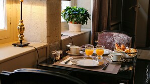 Una mesa de desayuno con una lámpara, una planta en maceta y un desayuno que incluye cruasanes y jugo de naranja.