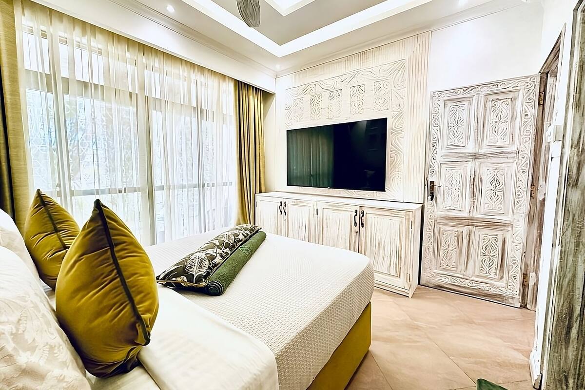 Une chambre à coucher avec un lit, des rideaux, une télévision et une armoire.