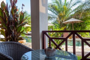 Une table avec un plateau en verre, agrémentée d’un vase décoratif, des chaises en osier, une piscine et, en arrière-plan, une végétation luxuriante.