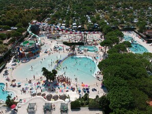 Ein großer Außenpoolbereich mit mehreren Wasserrutschen und ein Strandbereich mit Sonnenschirmen und Liegestühlen.