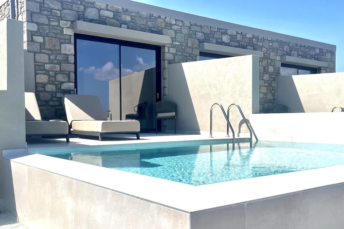 A modern outdoor pool area with stone walls, lounge chairs, and a clear blue pool.