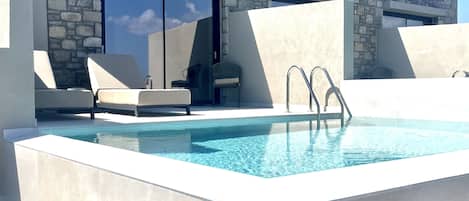 A modern outdoor pool area with stone walls, lounge chairs, and a clear blue pool.